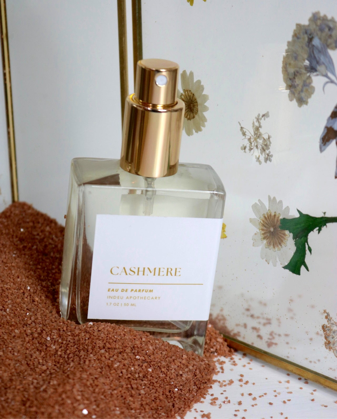A bottle of Cashmere Eau de Parfum with a gold-colored spray nozzle, placed on a surface with brown decorative elements and floral patterns in the background.