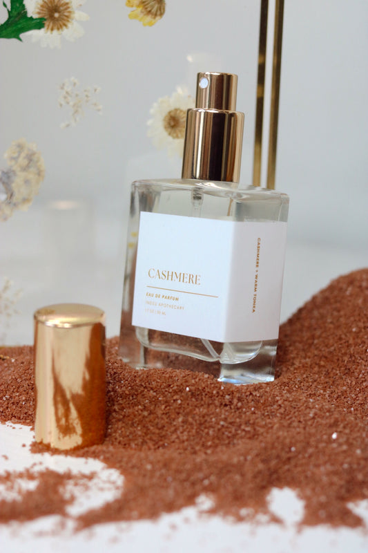 A bottle of Cashmere Eau de Parfum with a gold cap, displayed on a sandy surface with a label that reads 'CASHMERE'.